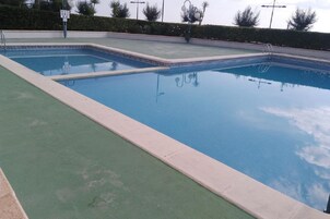 Una piscina rectangular con borde de azulejos y zona de cubierta en color verde.