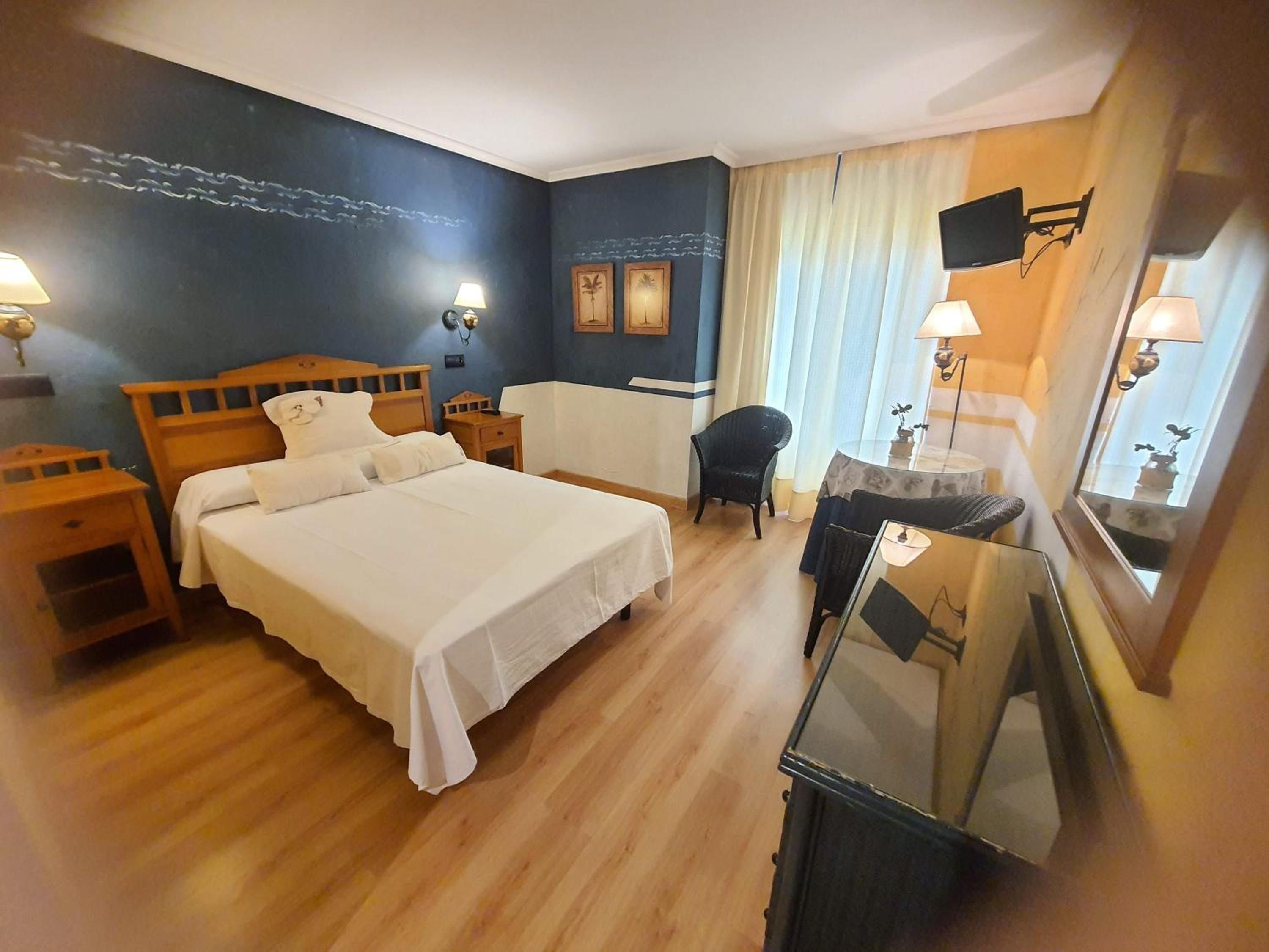 Una habitación de hotel con una cama grande, mesitas de noche, una silla, un escritorio y una televisión.