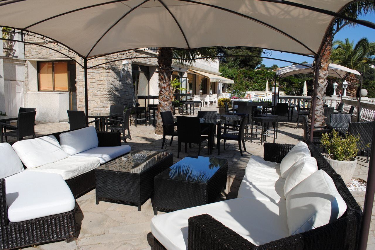 Eine Terrassengruppe im Freien mit Korbmöbeln, darunter Sofas und Tische, unter einem großen Sonnenschirm.