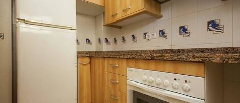 A kitchen with wooden cabinets, a white refrigerator, a stove, and a tiled backsplash with nautical-themed tiles.
