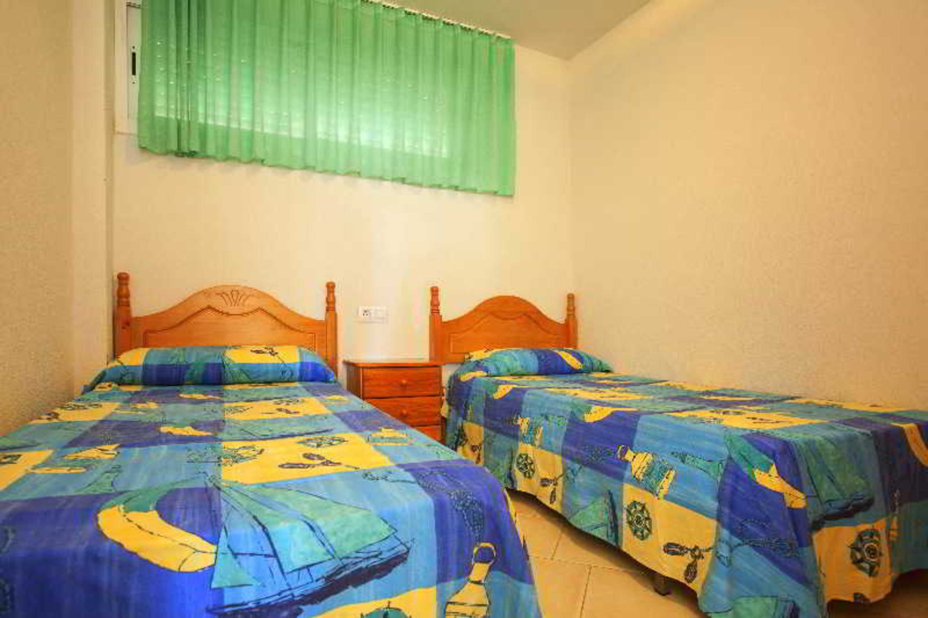 A room with two single beds, each with a wooden headboard, and a green curtain covering a window.