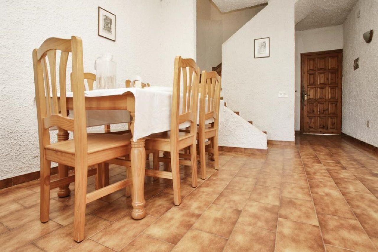 A dining area with wooden chairs and a table set for four, a staircase, and a wooden door.