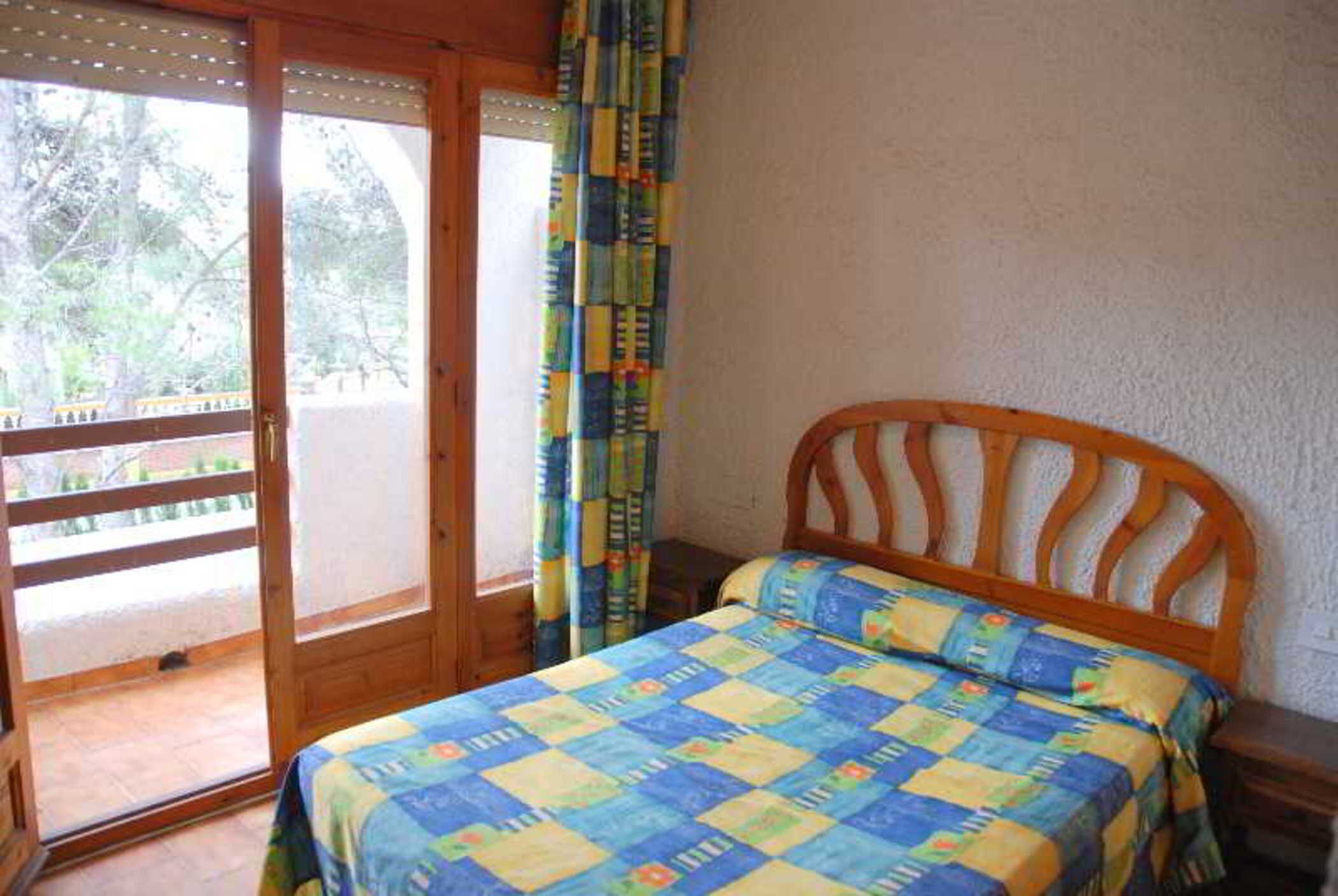 Une chambre avec un lit en bois, une fenêtre donnant sur un espace verdoyant et une porte coulissante menant à un espace extérieur.