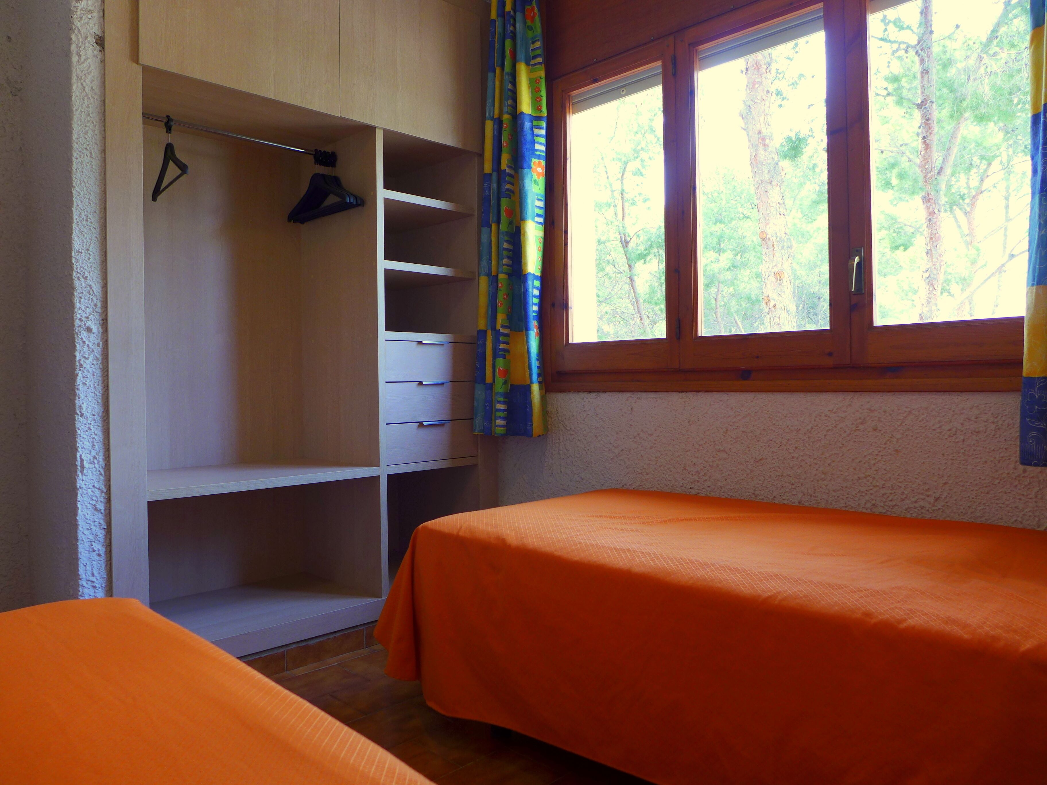 Quarto com uma cama de solteiro, guarda-roupa e janela com cortinas.