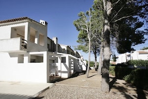 Una hilera de edificios blancos con balcones, un camino de grava y un árbol en primer plano.