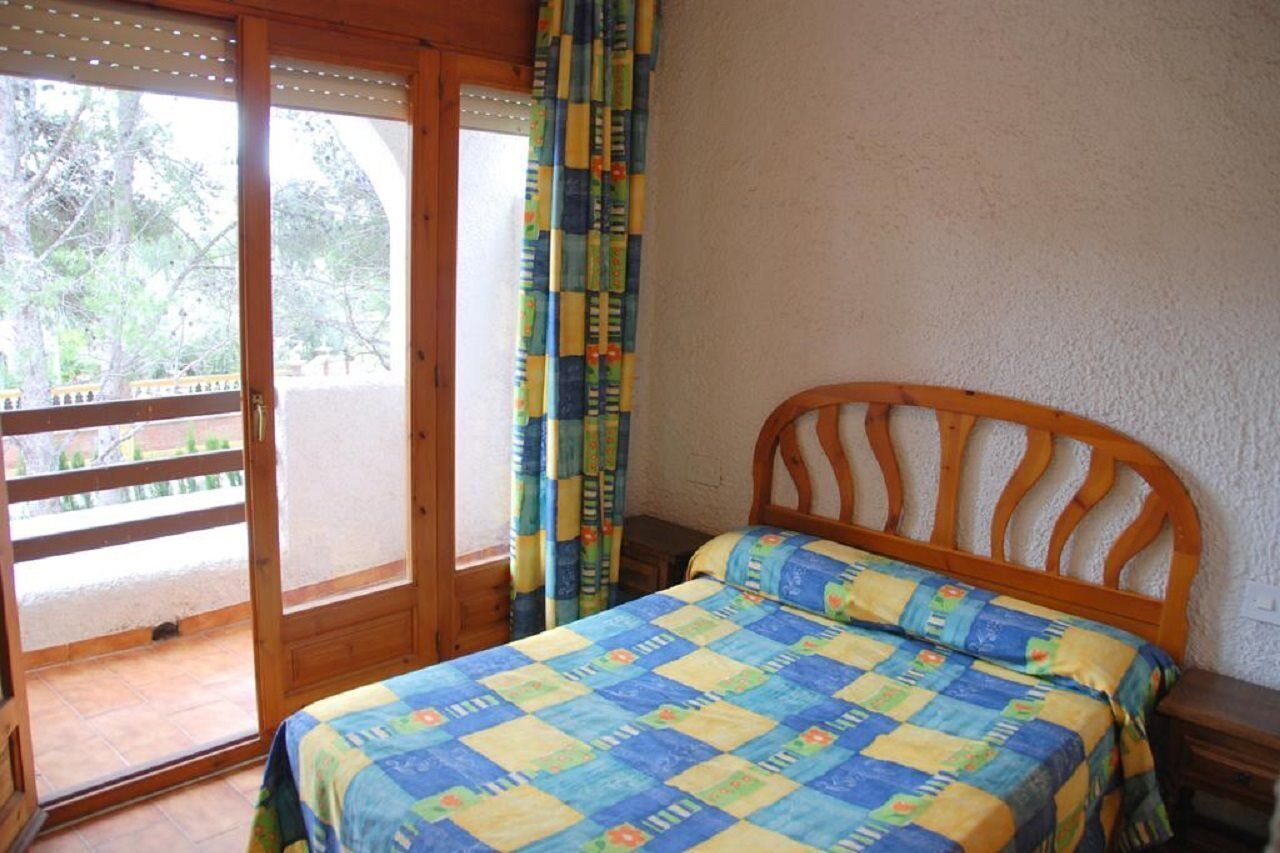 A bedroom with a wooden bed, a window with a view of trees, and a sliding glass door leading to an outdoor area.