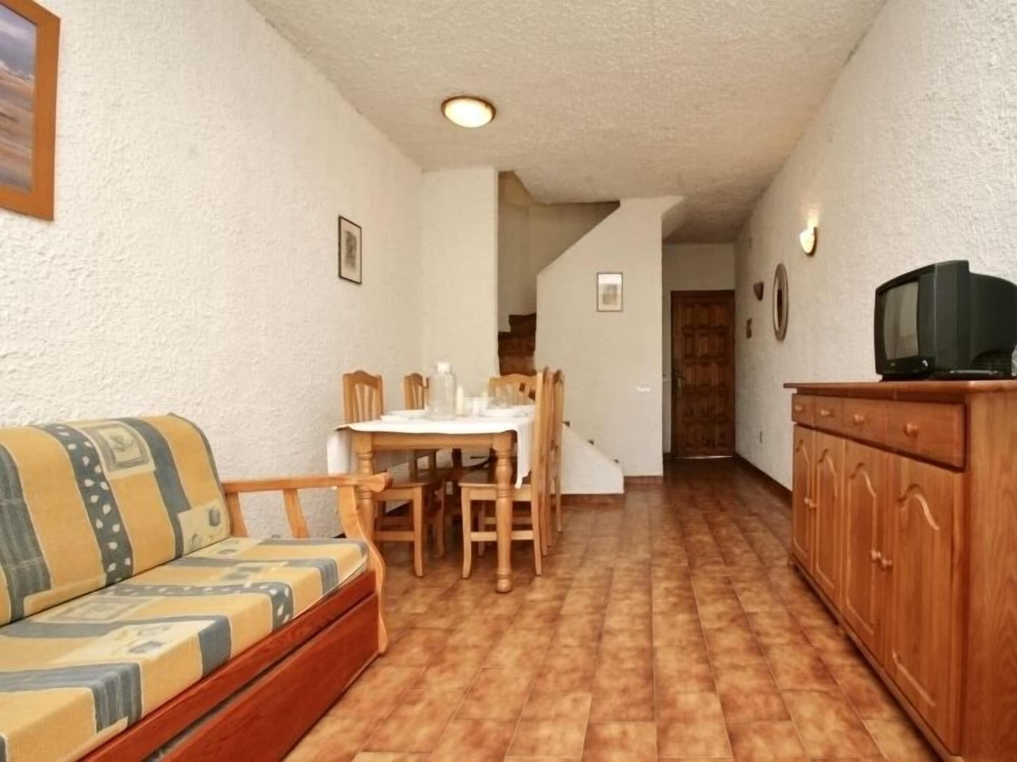 A compact living space with a sofa, dining table, chairs, and a television on a wooden cabinet.