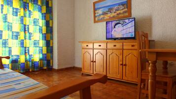 A room with a wooden cabinet, a television on top, a patterned curtain, and a wooden chair.