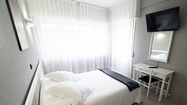 Habitació d'hotel amb llit, escriptori, cadira, televisió i finestra amb cortines.