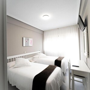 Habitación de hotel con dos camas, un escritorio, un televisor y una ventana con cortinas.