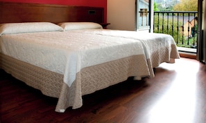 A double bed with a quilted cover in a room with wooden flooring and a red wall. - Hotel Virgen de Covadonga (Cangas de Onis)