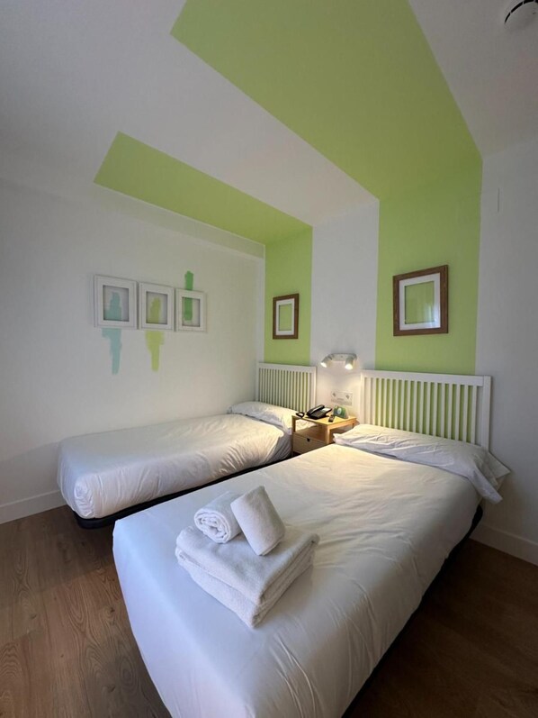 A hotel room with two beds, a wooden floor, and a green accent wall. - Hotel Virgen de Covadonga (Cangas de Onis)