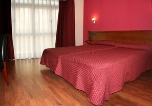 A room with a wooden floor, a bed with a red polka dot bedspread, and a wall-mounted light fixture. - Hotel Virgen de Covadonga (Cangas de Onis)