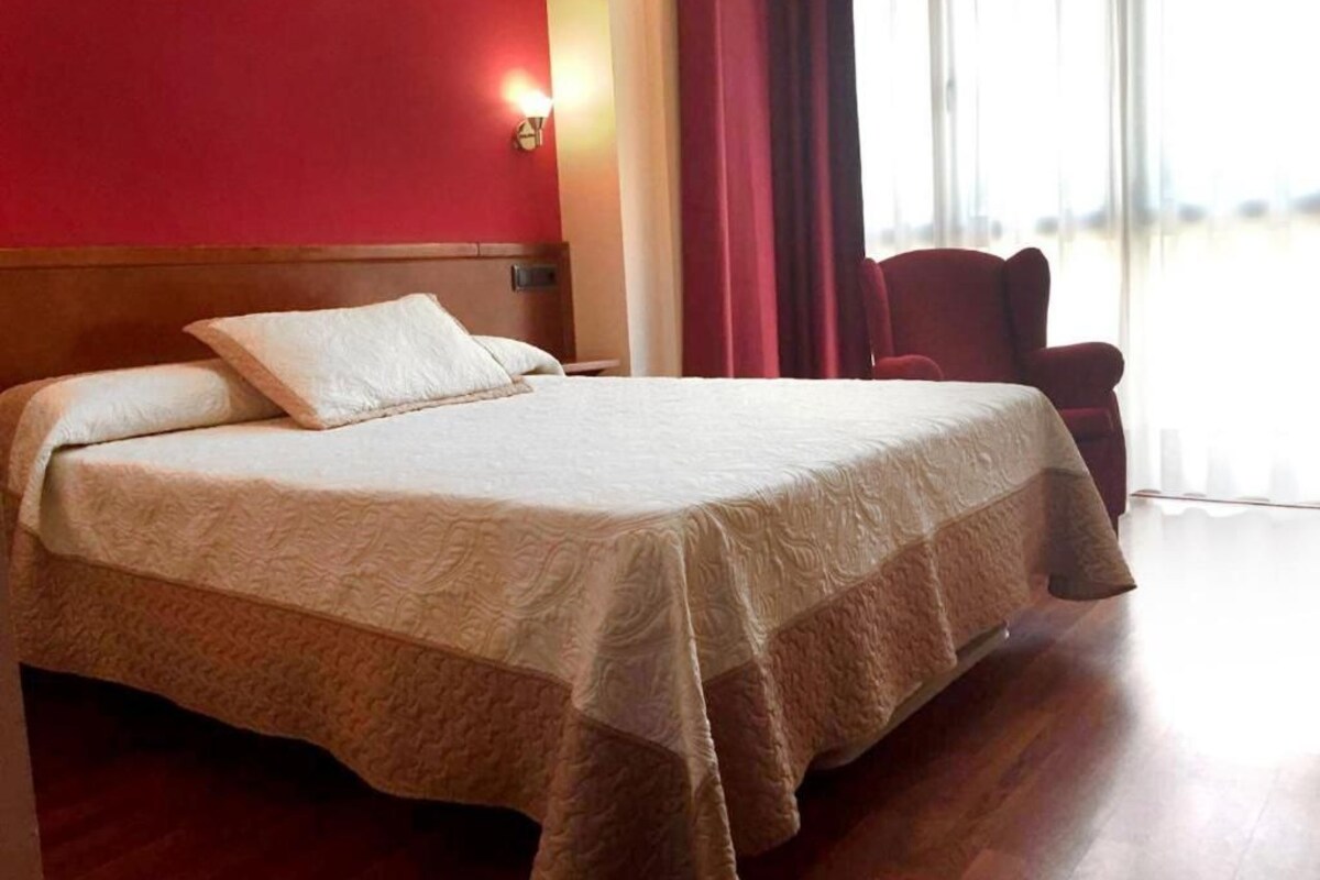 A hotel room with a large bed, a wooden headboard, a red wall, and a window with curtains.
