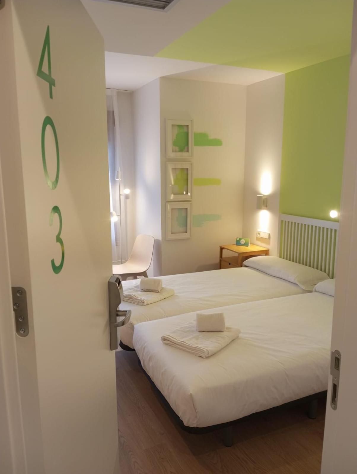 A hotel room with two beds, a chair, a nightstand, and a wall with a number.