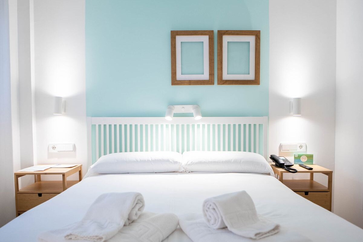 A hotel room with a bed, two bedside tables, a wall-mounted light, and a framed picture.