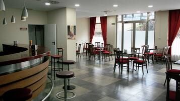 Un hall de hotel con mostrador de recepción, varias mesas de comedor con sillas y un mostrador de registro.