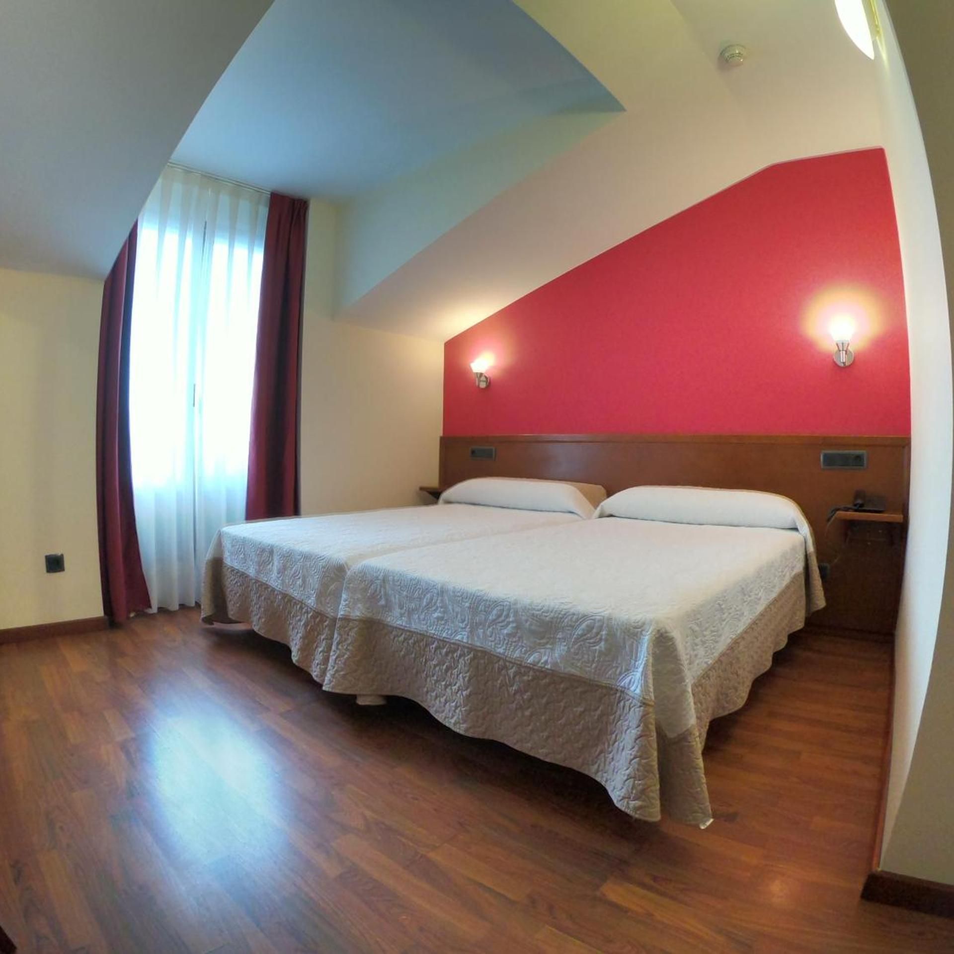 Una cama doble con cabecera de madera, una mesita de noche y una pared de acento roja.