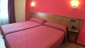 Habitación de hotel con dos camas, cabecero de madera, paredes rojas y dos luces fijadas a la pared.