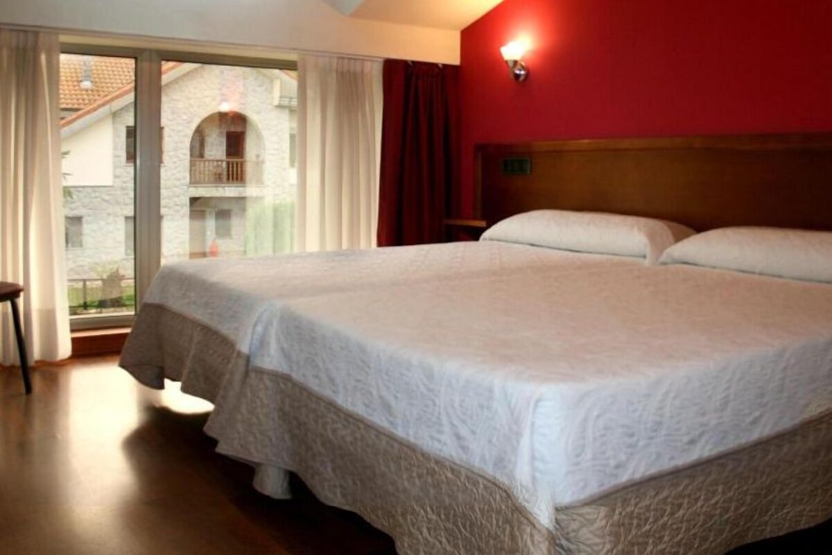 A double bed in a hotel room with a view of a building through a large window.