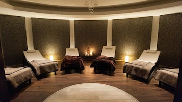 Relax in a serene spa room with a central table and candles, surrounded by four massage chairs.