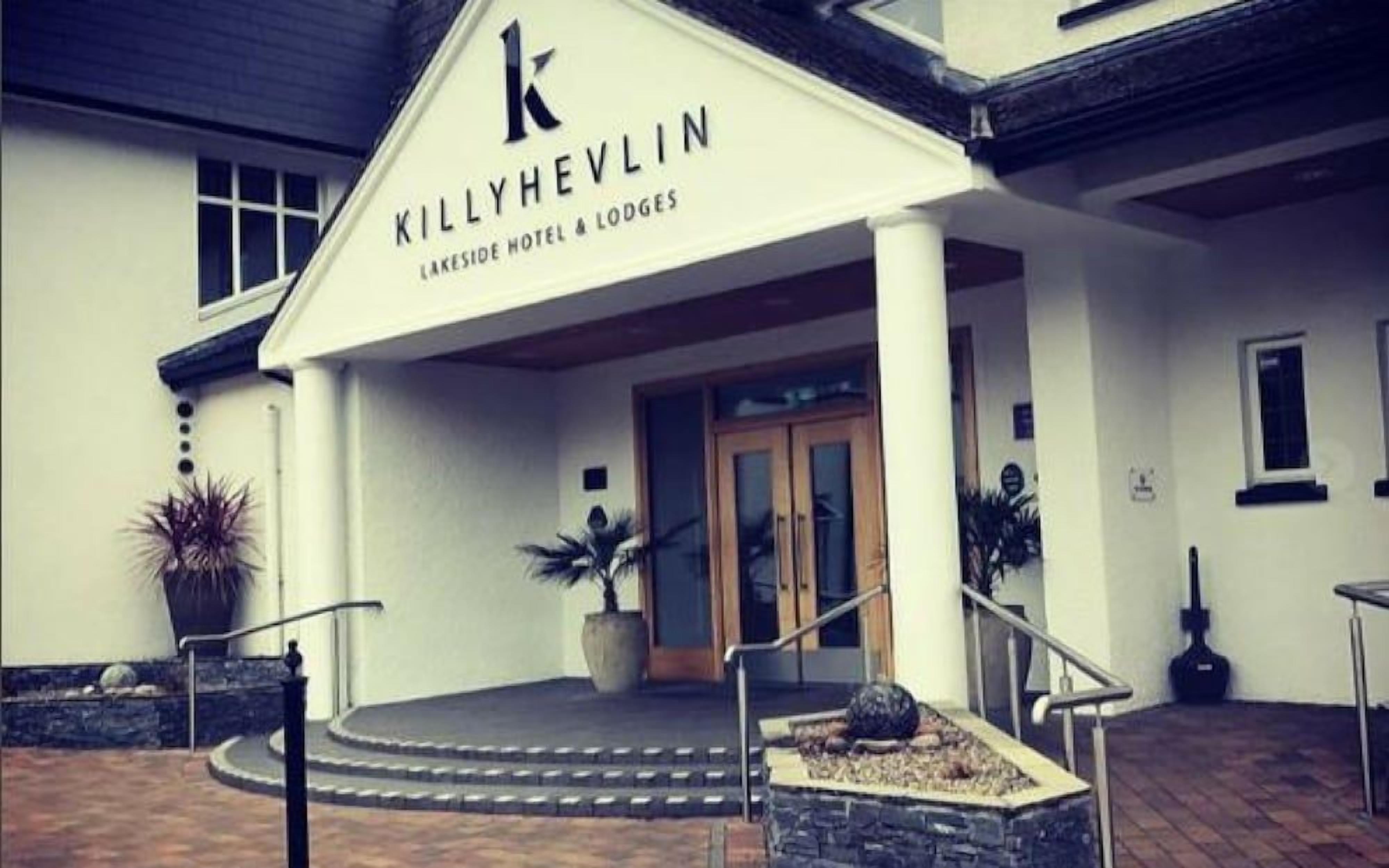 The entrance of the Killyhevin Lakeside Hotel & Lodges with a prominent 'K' logo, a set of stairs leading to the entrance, and potted plants.