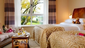 Ein Hotelzimmer mit zwei Betten, einer Couch, einem Esstisch mit Frühstücksangeboten, einer Handtasche und einem Teddybären.