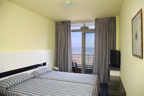 A hotel room with a bed, a television, and a balcony with a view. - Hotel Playamar Spa (Laredo)