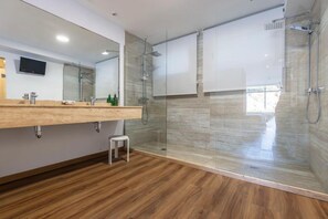 A modern bathroom with a glass-enclosed shower, a wooden vanity, a small stool, and a mounted television. - Hotel Sablon (Llanes)