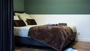 A neatly made bed with a patterned bedspread, a brown blanket, and two pillows.