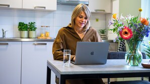 A person sitting at a table with a laptop and a glass of water. There is a vase with flowers on the table.