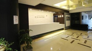 Un espace d’accueil avec un comptoir de réception blanc, une enseigne indiquant l’hôtel Jeju Airport, et un aménagement intérieur moderne avec un sol carrelé et une plante en pot.