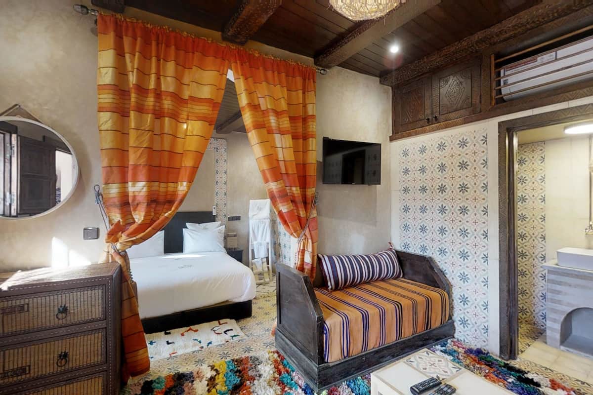 A bedroom with a bed, a sofa, a dresser, a mirror, and a bathroom with a sink and mirror.