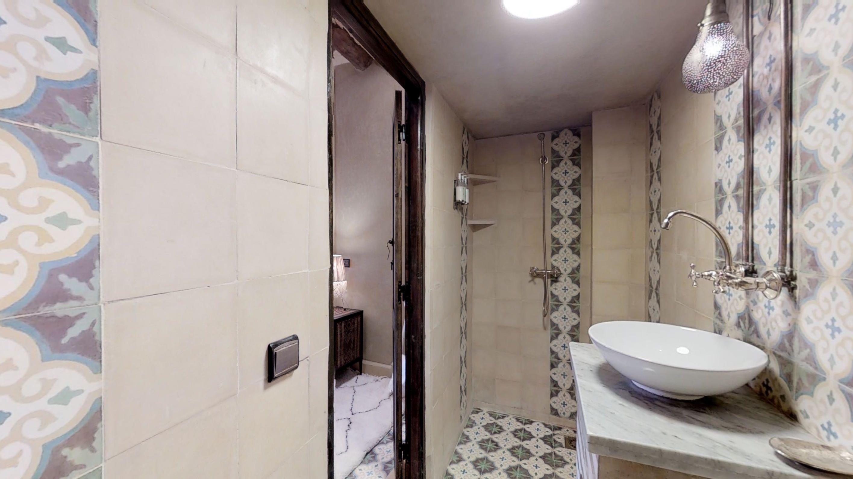 A bathroom with a white sink, a shower with a glass door, and patterned tiles on the walls.