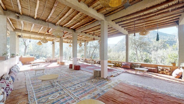 A spacious covered patio with a thatched roof, patterned rugs, and a view of a mountainous landscape. - Ferme By Ikalimo (Sti Fadma)