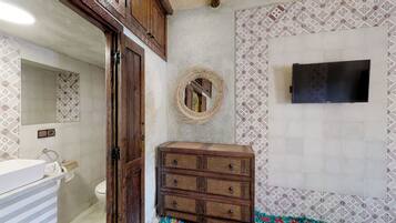 Un baño con un mueble de madera, un espejo, un televisor montado en la pared y azulejos estampados.