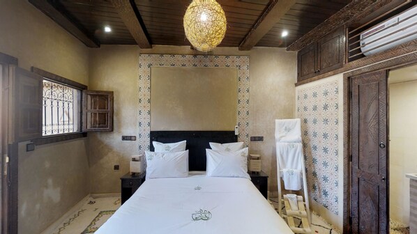 Un dormitorio con una cama grande, cabecera de madera, lámpara colgante, ventana con rejas y paredes con diseño.