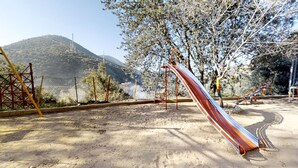 A playground with a slide and climbing structures, surrounded by trees and a hilly landscape. - Ferme By Ikalimo (Sti Fadma)