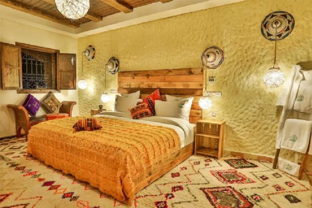 A cozy bedroom with a wooden headboard, a patterned bedspread, and a decorative rug.