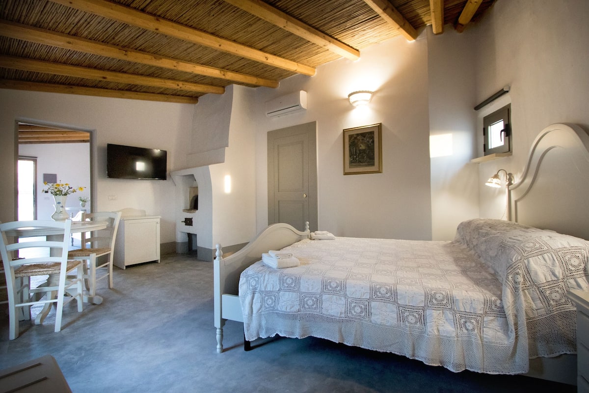 A bedroom with a bed, a desk, and a chair. There is a television on the wall, a door, and a window.