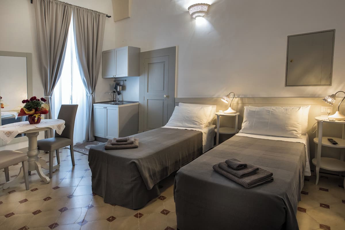 A hotel room with two single beds, a desk with a chair, a small kitchenette, and a bathroom.