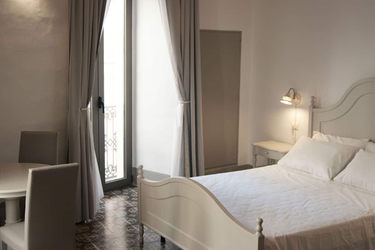 A hotel room with a bed, a bedside table, a chair, and a window with curtains.