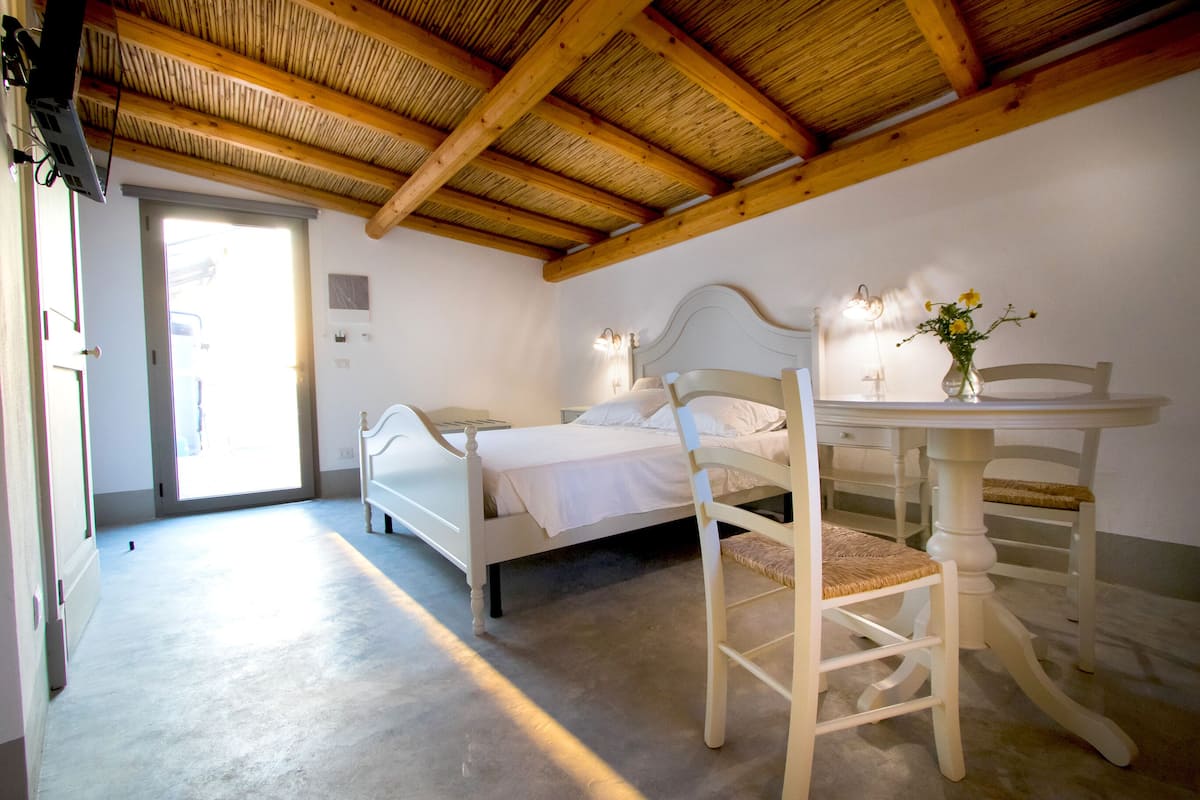 A bedroom with a bed, a chair, a table, and a vase with flowers.