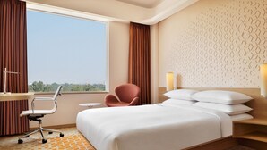 Habitación de hotel con una cama grande, un escritorio, una silla y vistas a la ciudad.