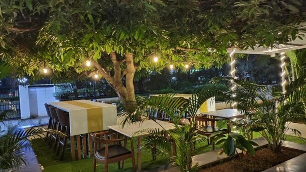 Un área de comedor al aire libre con una mesa y sillas, rodeada de follaje e iluminación colgante.