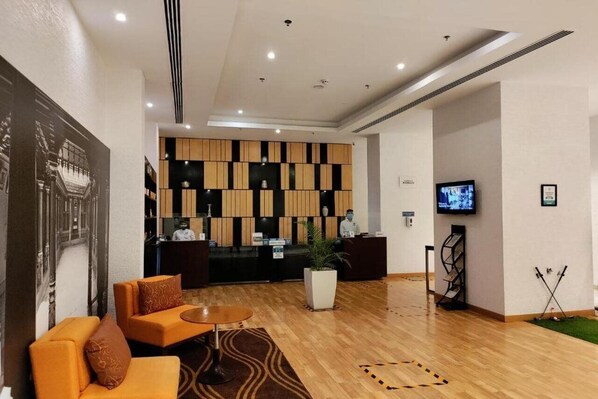 Un hall de hotel con mostrador de recepción, zona de estar y televisor.