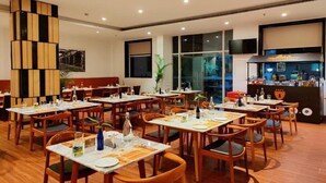 Un restaurante con mesas y sillas de madera, una barra negra con un letrero y amplios ventanales.