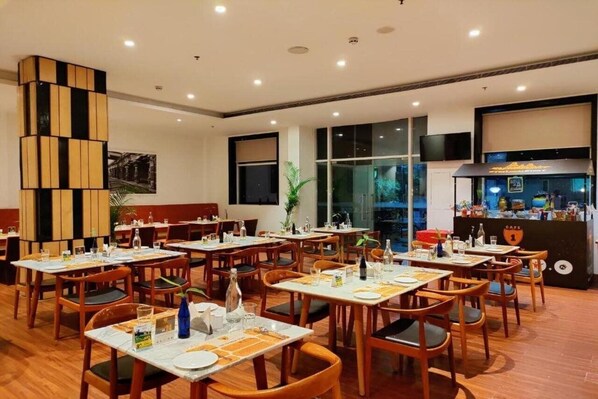 Un restaurant avec des tables et des chaises en bois, un comptoir noir avec une enseigne et de grandes fenêtres.