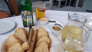 A table with a plate of sliced bread, a bottle of beer, a glass of beer, and a pitcher of white wine. - Haridimos Apartments (Platanias)