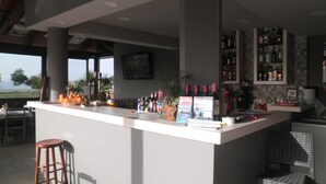 A bar area with a counter, stools, and a view of the ocean. - Haridimos Apartments (Platanias)